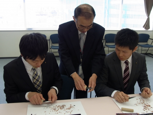 小刀で鉛筆を削るのは初めてと答える新人社員に、先輩たちが直接指導