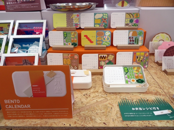 日本文化の一つでもある弁当（BENTO)をカレンダーへ「べんとうカレンダー」。12カ月（12種）のメニューは行事に合わせて四季折々、旬の材料を取り入れた、代表的な日本食弁当。カード裏面にはお弁当の献立。「おてもと」のQRコードからレシピもご覧いただけます。一九堂